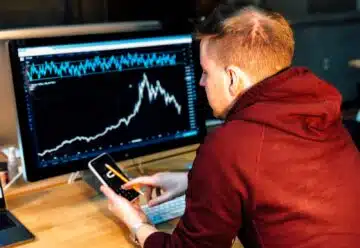 man holding black smartphone with flat screen monitor in front