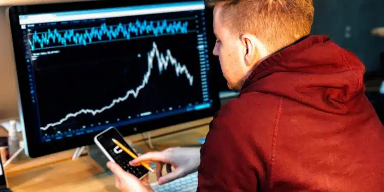 man holding black smartphone with flat screen monitor in front